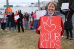 Teacher holds up a picket sign that says We Love Your Kids