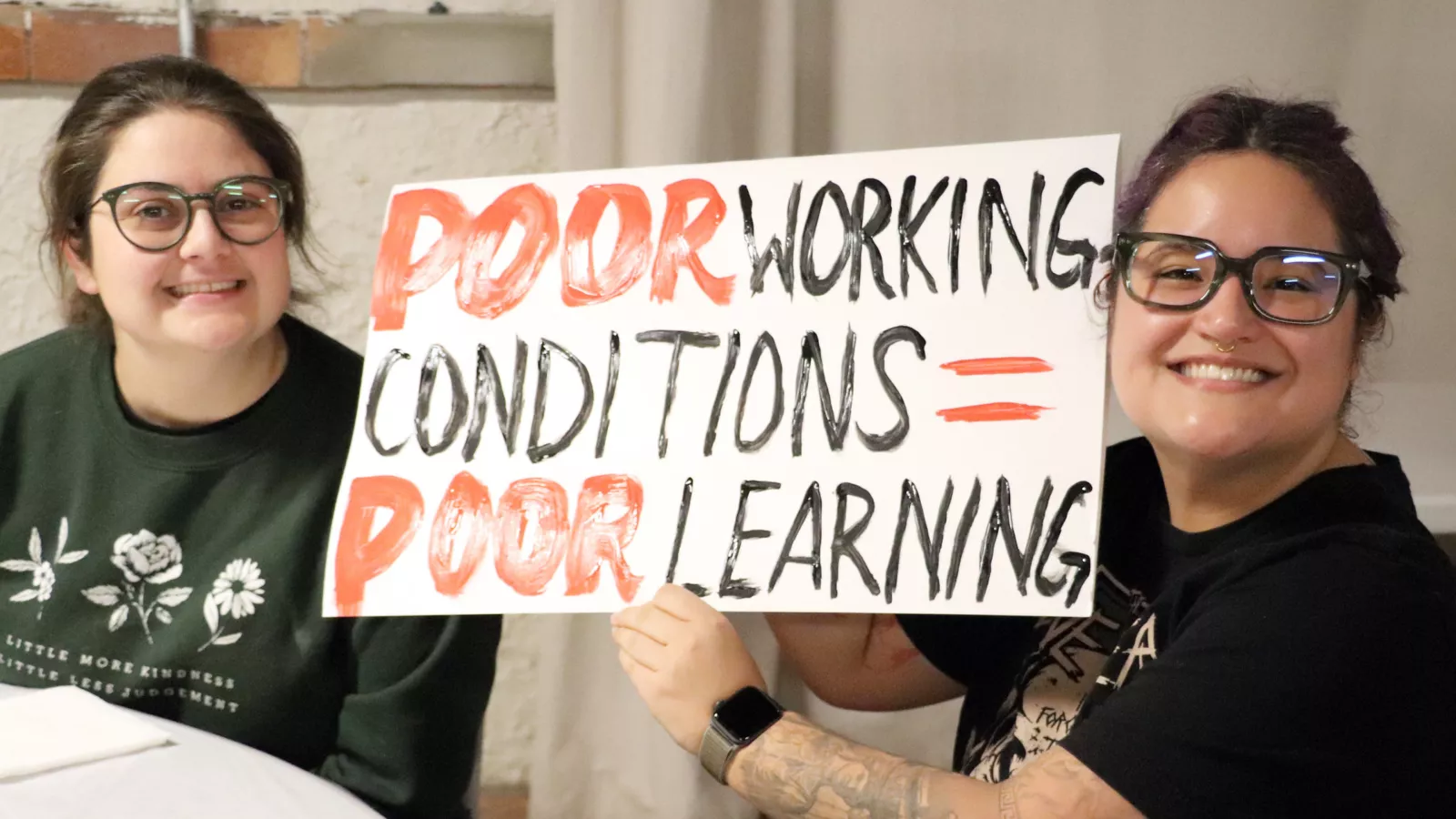 two members with sign that says "poor working conditions = poor learning conditions"