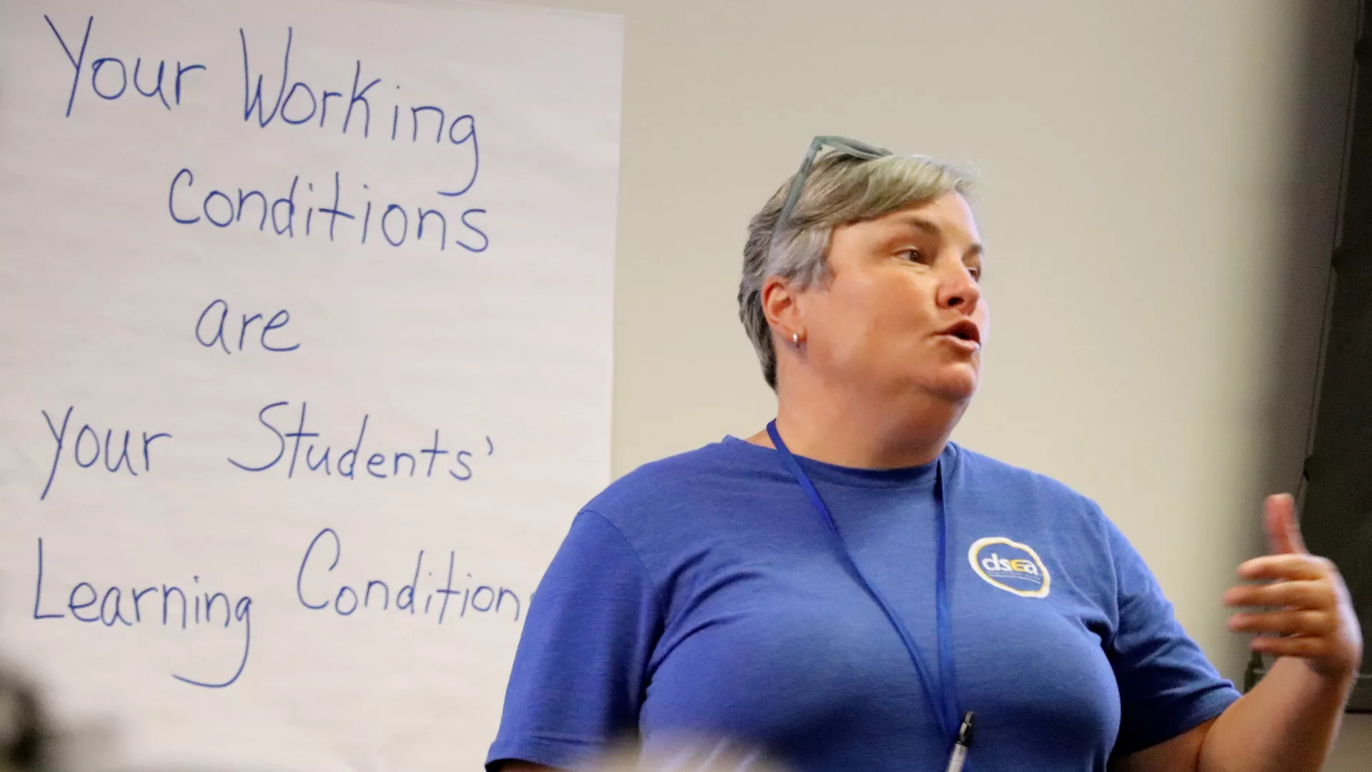 Christina Paraprofessional Association President Gretchen Loose stands in front of a whiteboard that says Your Working Conditions Are Your Students' Learning Conditions