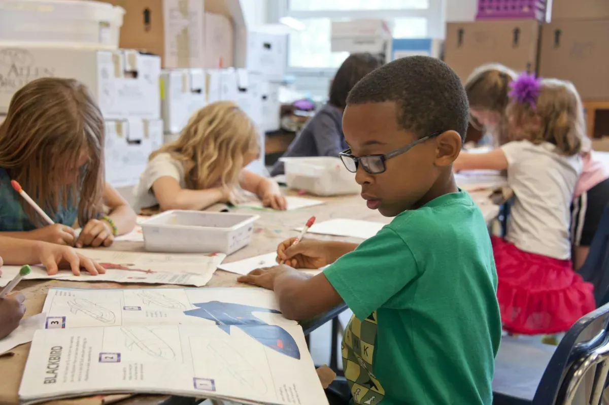 A young boy with glasses does school work in a classroom